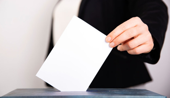 Gros plan sur une enveloppe blanche qu'une femme glisse dans une urne pour voter
