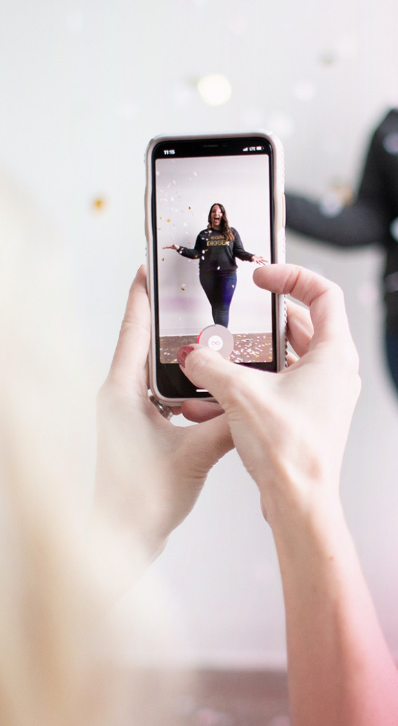A woman taking a photo of an influencer on a pink background