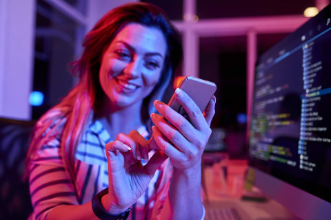 A woman scrolls on her mobile phone while smiling.