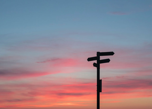 A silhouette of a signpost with a sunset in the background