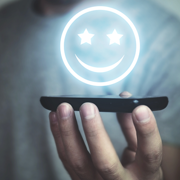 A glowing emojicon hovering above a mobile phone held by a man.