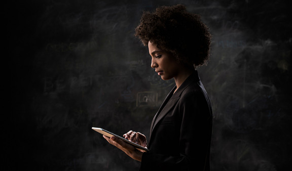 Une femme africaine habillée d'un costume sombre et placée de profil consulte une tablette