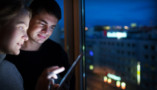 Deux personnes regardent des informations sur tablette dans un bureau face à une ville éclairée