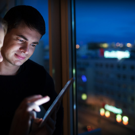 Deux personnes regardent des informations sur tablette dans un bureau face à une ville éclairée