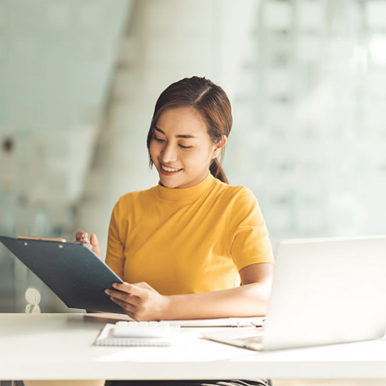 Jeune femme asiatique souriante en pull jaune qui regarde le cours de la bourse sur un écran de tablette