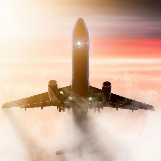 Un avion vu du dessous vole à travers un nuage dans un ciel aux couleurs du coucher du soleil