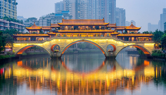 Un pont lumineux traverse une rivière dans une ville d'Asie